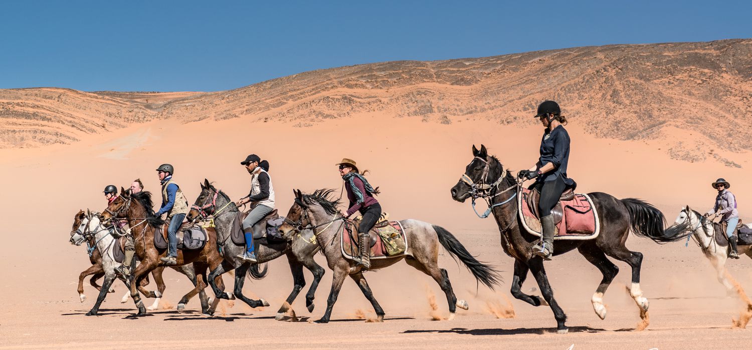 Group horseback riding expedition through the Moroccan desert with dramatic mountain backdrop